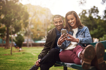 Aufkleber - What do you think about this photo. Shot of a cheerful young couple sitting down on a bench while using a phone together outside in a park.