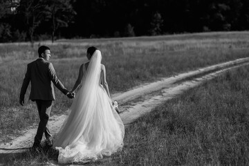 Loving wedding couple in the forest for a walk. The bride has a beautiful long veil and black hair. sunny summer day