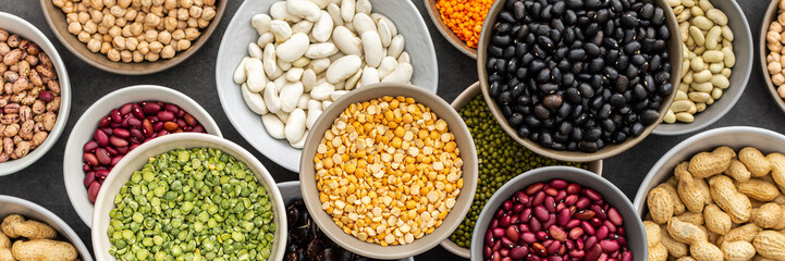 Banner of different types of legumes in bowls, green with yellow peas and mung beans, chickpeas and peanuts, colored beans and lentils, top view