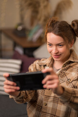 Poster - Girl gamer enthusiastically plays a video game on a portable game console at home, in the room. Leisure, day off, tourism, travel, hotel, game on the road. Cyberspace, cybersport, gaming.