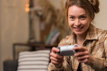 Wall Mural - A fair-haired girl gamer with a joystick plays a video game at home, in a room. Close-up. Virtual reality, recreation, entertainment, holidays, communications, fun adventure video games with friends.