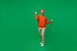 Full body young excited happy man 20s wear orange sweatshirt hat doing winner gesture celebrate clenching fists say yes isolated on plain green background studio portrait. People lifestyle concept