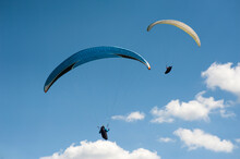 Two Paragliders Flying In The Blue Sky Against The Background Of Clouds. Paragliding In The Sky On A Sunny Day.