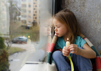 a little ukrainian girl prays for the freedom of ukraine and holds a candle in her hands. a sad girl
