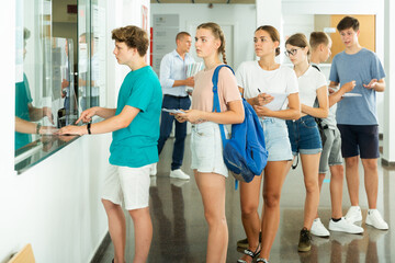 Group of teenage students queuing at front office on college campus, awaiting registration for classes and lessons at start of new semester