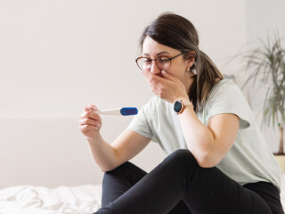 Wall Mural - the woman found out about an unwanted pregnancy. A woman with a pregnancy test in her hands is sitting on the bed in her apartment