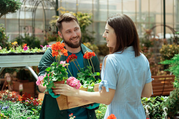 Worker helping female customer to buy flowers in garden center