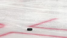 Puck Lies On Scratched Ice With Red Marking Lines While Players Skate Past At Hokey Tournament Closeup Slow Motion