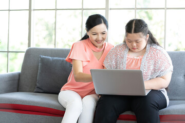 Wall Mural - mother using laptop computer and a girl with down syndrome or her daughter, smiling and enjoying on sofa