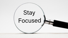 Phrase Stay Focused Through A Magnifying Glass On A Light Background