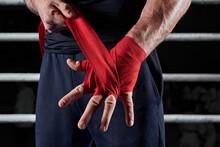 Red Bandages On The Hands Of A Kickboxer Against The Background Of The Ropes Of The Ring. The Concept Of Mixed Martial Arts.