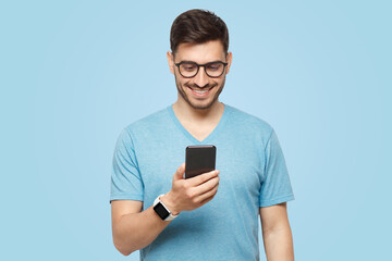 young handsome man in blue t-shirt holding smartphone and looking at phone screen