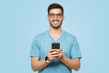 Young handsome man in blue t-shirt and wearing glasses, standing with phone in hands