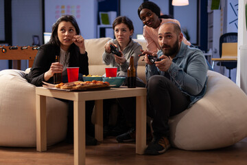 Wall Mural - Diverse group of people playing video games on console, using controller on tv at office celebration with drinks and food. Colleagues enjoying after work party with alcoholic beverage and game.