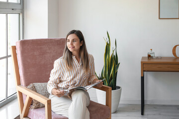 Sticker - Young woman with magazine sitting in comfortable armchair at home