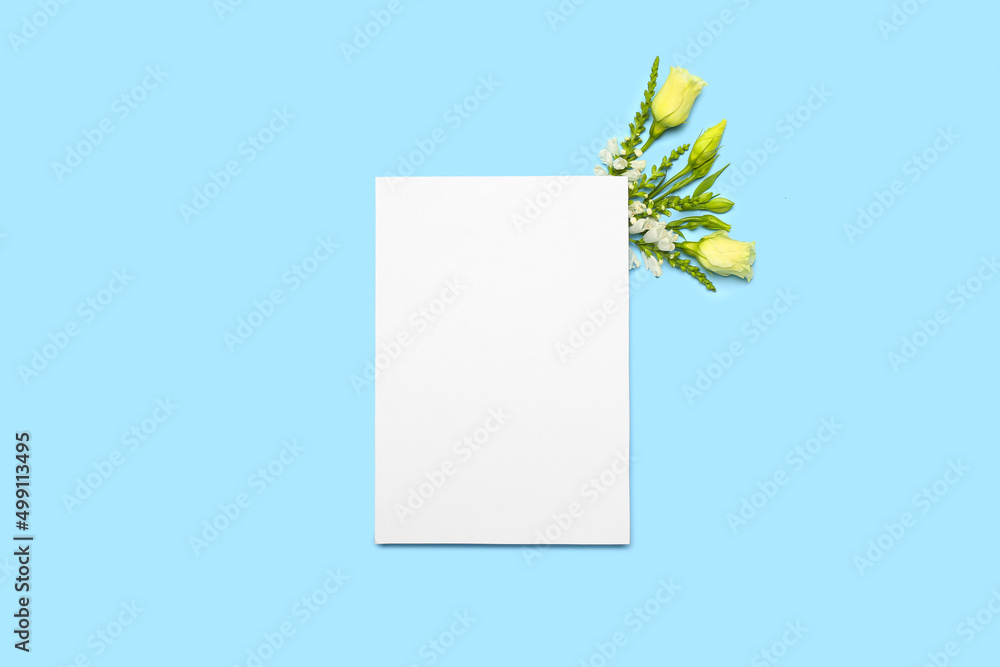Blank sheet of paper and flowers on blue background