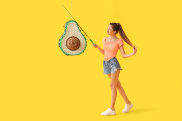 Wall Mural - Happy young woman breaking Mexican pinata on yellow background