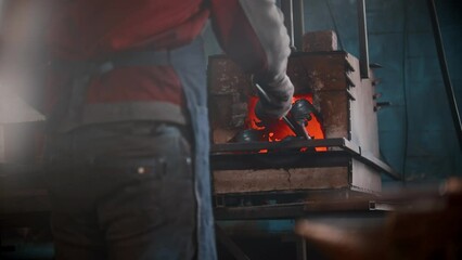 Wall Mural - Blacksmith workshop - a man puts metal thing in the oven using pincers