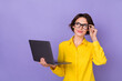 © deagreez - Photo of cute millennial lady hold laptop look up wear yellow outfit eyewear isolated on violet color background