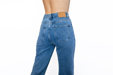 Fashionable blue jeans with a high fit on a slender young woman standing with her back isolated on a white background. Rear view. Beauty and fashion concept