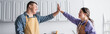 © LIGHTFIELD STUDIOS - Cheerful friends with down syndrome in aprons giving high five in kitchen, banner.