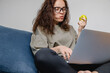 Beautiful young adult woman eats healthy food green apple and using her laptop at home, healthy eating lifestyle.
