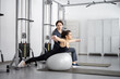 © rh2010 - Woman doing exercises on fitness ball and dumbbells with rehabilitation specialist at the gym. Concept of physical therapy for back strengthening and recovery. Idea of recovery after pregnancy