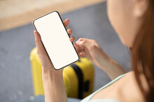 Back View Of Girl Holding Smartphone With White Blank Screen Mockup. Traveler With Phone At The Airport With Passport And Suitcase.