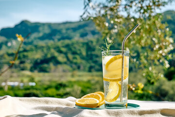 Summer refreshing lemonade drink or alcoholic cocktail with ice, rosemary and lemon slices on the table in the garden. Fresh healthy cold lemon beverage. Water with lemon.