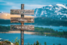 Give Others Grace Text Quote Written On Wooden Signpost Outdoors In Nature With Lake And Mountain Scenery In The Background. Moody Feeling.