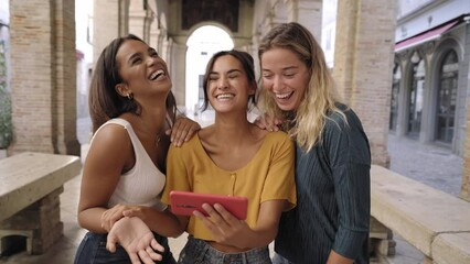 Wall Mural - Three happy women using mobile phone outdoors. Group of smiling female friends watching social media at smartphone