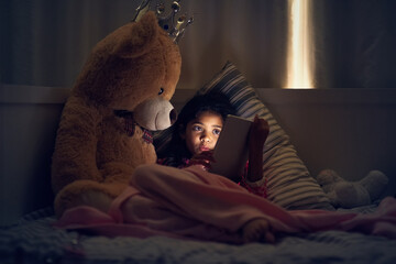 Wall Mural - Watching her favourite cartoons before bed. Shot of a little girl using a digital tablet while lying in bed with her teddy at night.