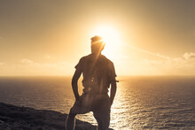 Male Hiker On A Mountain Cliff Facing The Ocean Sunrise. Peace, Adventure And Freedom In Nature. 