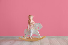 Adorable Baby Girl With Rocking Horse Near Pink Wall