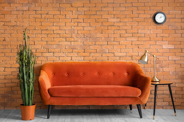 Table with lamp, red sofa and big cactus near brick wall