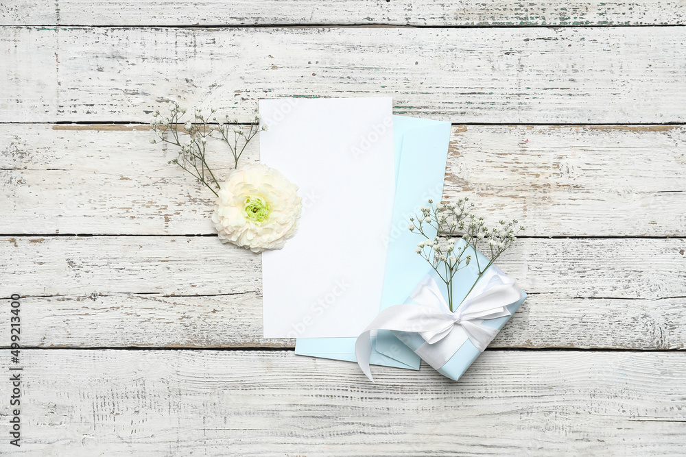 Envelope with card, gift and flowers on white wooden background