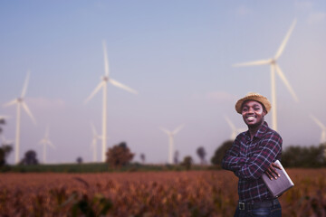 african farmer standing and holding digital tablet on corn farm with wind turbine in background.conc