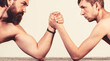 © Yevhen - Two man's hands clasped arm wrestling, strong and weak, unequal match. Heavily muscled bearded man arm wrestling a puny weak man. Arms wrestling thin hand, big strong arm in studio