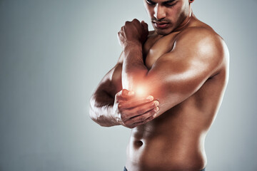 Wall Mural - No lifting weights for a while. Cropped shot of a sporty young man holding his elbow in pain against a grey background.