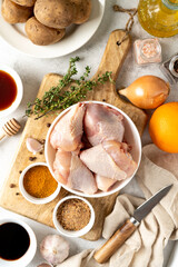 Wall Mural - Raw chicken legs, potatoes and spices on a light gray culinary background. Raw poultry meat, vegetables and seasonings are prepared for pickling. Top view	