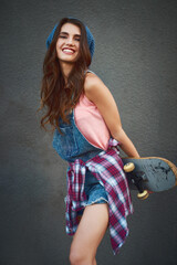 Poster - The sweetest skateboarder youll ever meet. Shot of an attractive young female skater holding a skateboard behind her back while standing against a grey background.