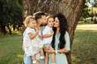 © shunevich - Happy parents with little kids at the park, caring dad hold in arms adorable daughter, beautiful mom hold joyful son, loving husband gentle kiss lovely wife, family concept