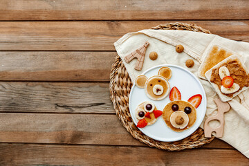 Wall Mural - Creative meal for a child, pancake with strawberry, funny food over wooden background. Top view, flat lay