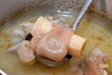 Selective focus of an Arabic Egyptian cuisine of kawareh soup ( trotters soup ) that is full of collagen and Gelatin, cooked cow feet in a cooking pot with onion, cow boneless trotters with its soup