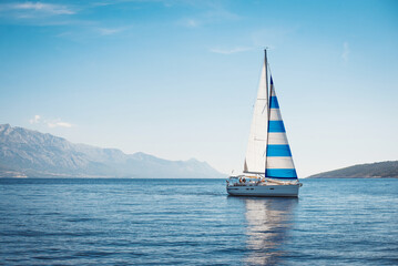 Wall Mural - A white yacht with Greek flag sails at sea against the blue sky and mountains