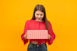 Smiling and happy young girl with gift box in her hands. Unexpected gift. Deep yellow background.