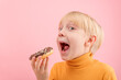 © somemeans - Towheaded boy wants to bite donut with chocolate icing. Close up portrait of child with doughnut on pink background.