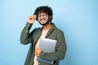 © Kateryna - Smart handsome positive indian or arabian millennial guy, with glasses, student or freelancer, holding a laptop in hand, standing on isolated blue background, looking at the camera, smiling friendly