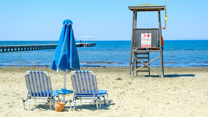 Two blue sun loungers standing on a blue flag beach. Enjoying the sea on the beach. Sun umbrella in blue color. Blue sun beds on the sea side.