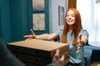 © dikushin - Cheerful excited young woman receiving paper boxes with pizza from unrecognizable courier male on doorway at home. Rear view of delivery man delivering boxes with food to female client at apartment.